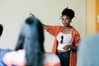 Young female teacher pointing on whiteboard while teaching students in classroom