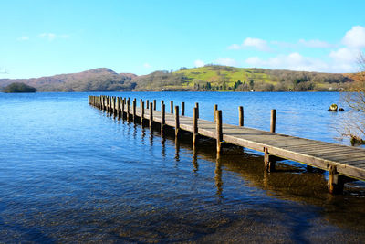 Wooden pier over lake against blue sky