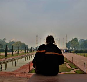 Rear view of woman sitting on retaining wall against sky