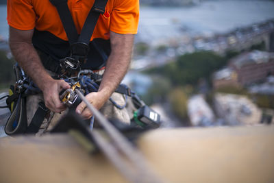 Midsection of man hanging on rope with safety harness