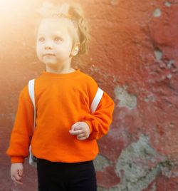 Full length of cute boy standing against orange wall