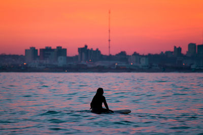 Silhouette man in sea against sky during sunset