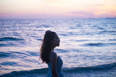 Woman looking at sea shore against sky during sunset