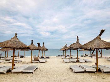 A beach with empty wooden sunbeds and thatched roof umbrellas on a day with dark storm clouds