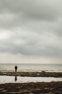 Rear view of woman at calm sea against cloudy sky