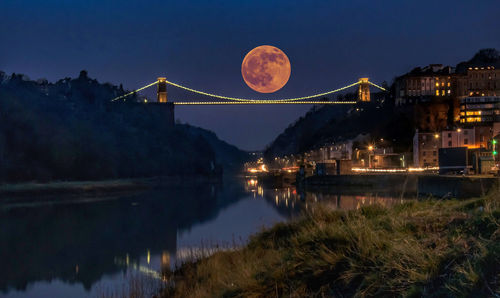 Illuminated bridge over river against sky at night