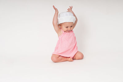 Happy baby sitting with arms up against white background