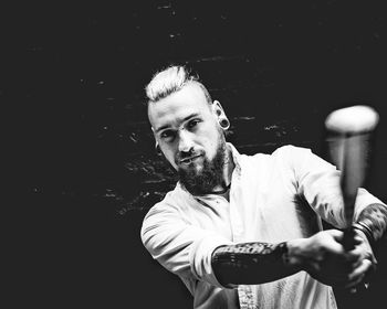 Portrait of punk holding baseball bat against wall in darkroom