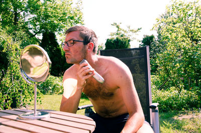 Shirtless man trimming beard in yard