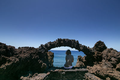 Rear view of man looking at sea against clear sky