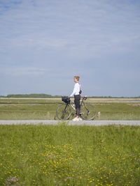 Rear view of man riding bicycle on field against sky