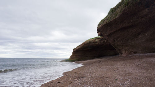 Rock formations at beach against sky