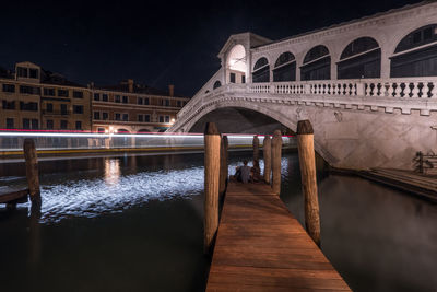 Rear view of couple sitting on pier by canal at night