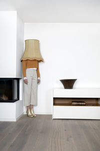 Woman with lamp shade on head standing in corner of wall at home