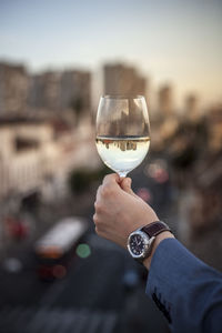 Cropped hand of businessman holding wine in glass against city