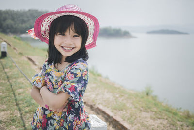 Portrait of smiling girl wearing hat standing by lake