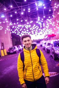 Portrait of smiling young man standing in illuminated city at night