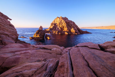 Scenic view of rocks in sea against clear blue sky