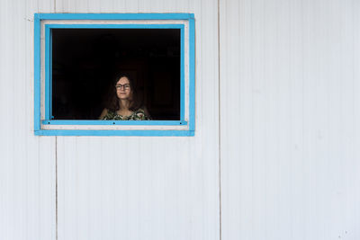 Portrait of woman looking through window of door