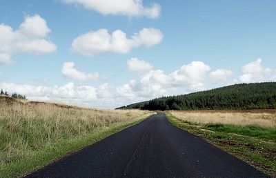 Empty road amidst field against sky