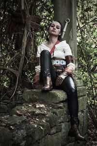 Portrait of smiling young woman sitting on tree trunk in forest