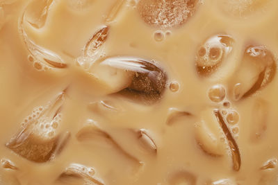 Close-up of cold latte drink with ice cubes, iced coffee texture.