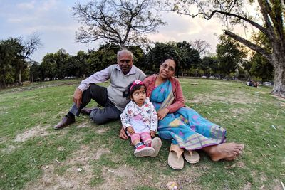 Full length portrait of family sitting on grass in park against trees and sky