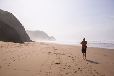 Rear view of man walking at beach against clear sky