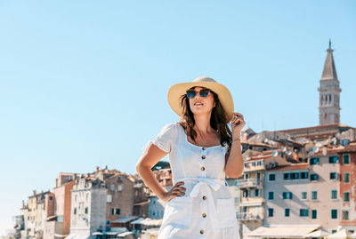 Woman wearing hat standing against buildings