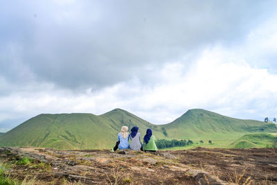 Rear view of three women sitting on mountain against sky