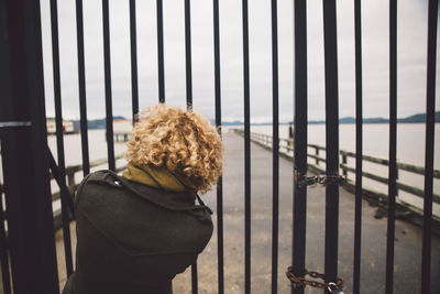 Rear view of woman looking through closed gate at pier