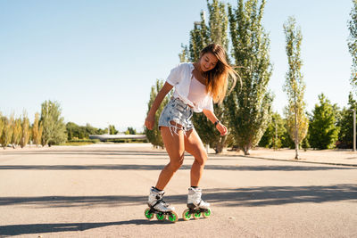 Side view of fit female in rollerblades showing stunt on road in city in summer