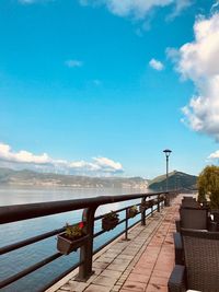 Pier on footpath by street against blue sky