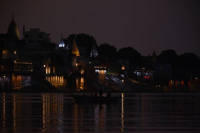 Illuminated buildings by river against sky at night