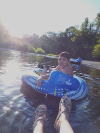 Boy sitting by lake against sky