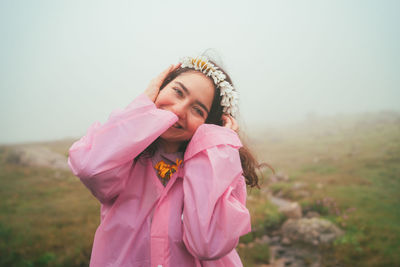 Portrait of young woman wearing hat made of flowers standing against sky