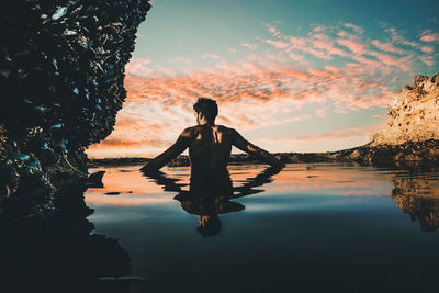 Reflection of man in lake against sky during sunset