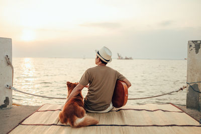 Rear view of woman with dog sitting on sea shore against sky