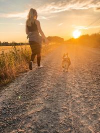Rear view of woman with dog on street during sunset