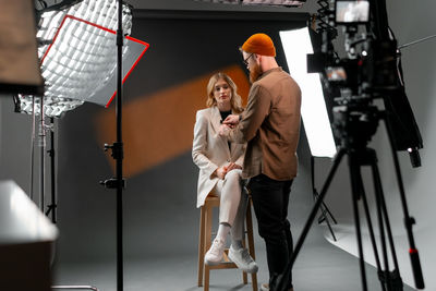 A man and woman chat on camera with stage equipment