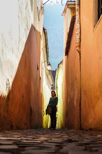 Surface level image of mid adult woman standing on alley amidst buildings in city