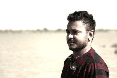 Young man looking away while standing at beach