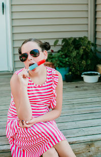 Girl wearing sunglasses sitting outdoors eating a popsicle 