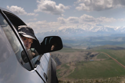 A young woman or girl enjoys the view from the window of an suv car on the mountains in the clouds