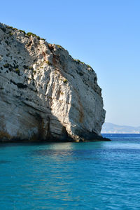 Rock formation in sea against clear blue sky