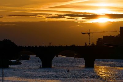 Silhouette bridge over river against sky during sunset