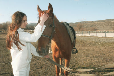 Young woman stroking horse while standing in animal pen