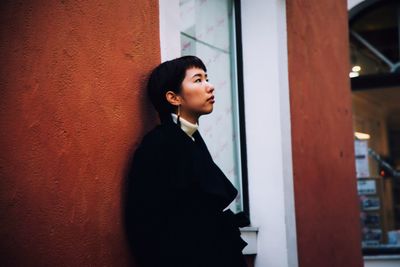 Young woman looking away while standing against wall