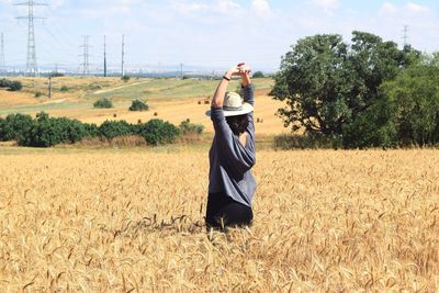 Rear view of person standing in field against cloudy sky