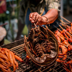 Midsection of vendor cooking seafood on barbecue grill
